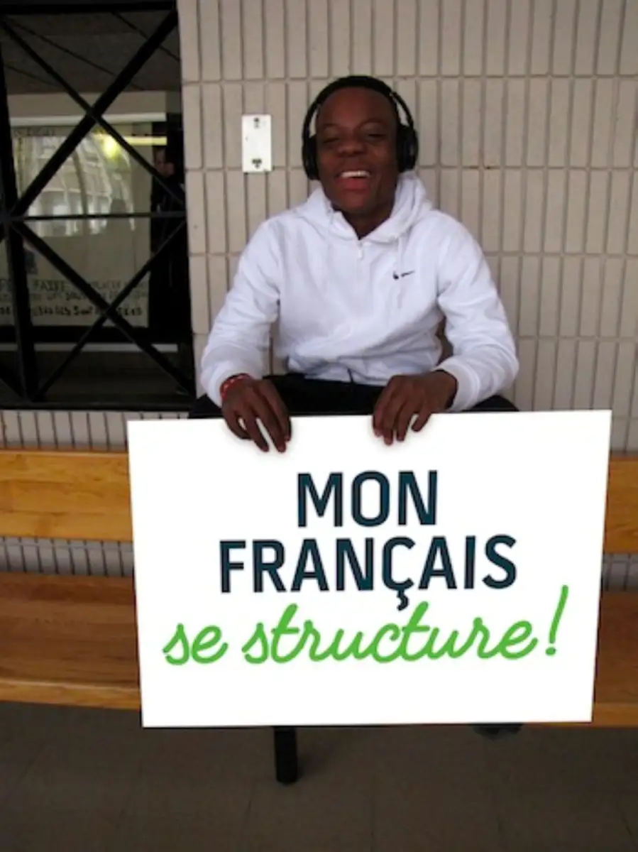 Étudiant qui tient une pancarte "Mon français se structure"