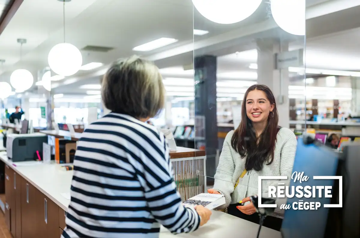 Personne étudiante souriante qui reçoit les services d'une personne à la bibliothèque.