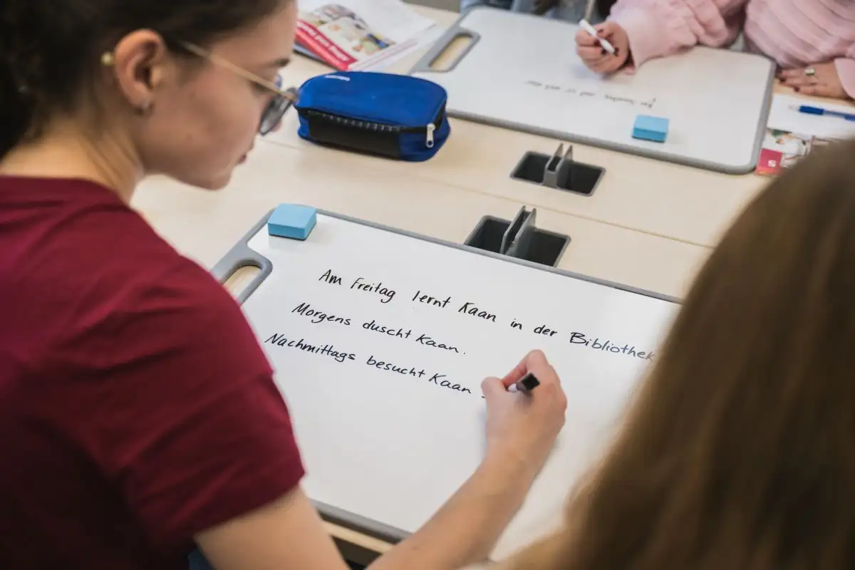 Personne étudiante assise à table qui écrit en allemand sur un tableau blanc