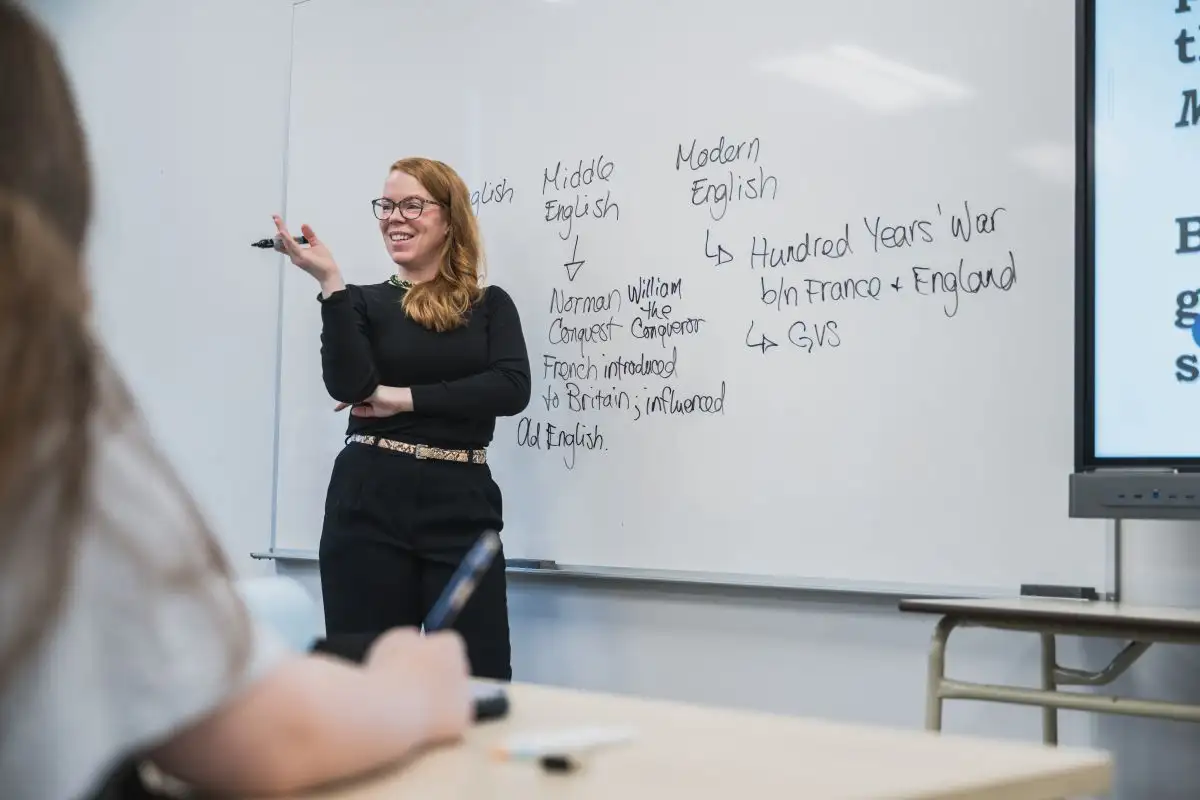 Personne enseignante qui explique son cours devant un tableau blanc