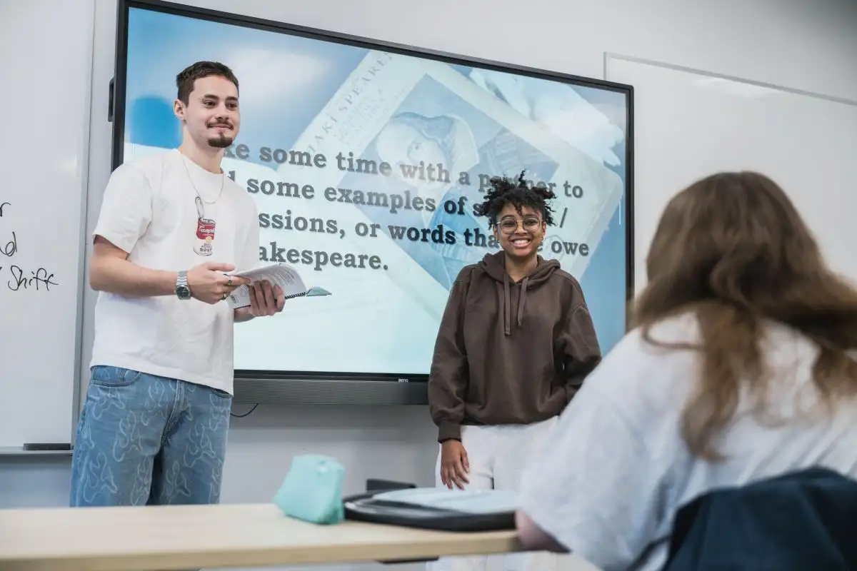 Deux personnes étudiantes qui présentent devant un tableau interactif