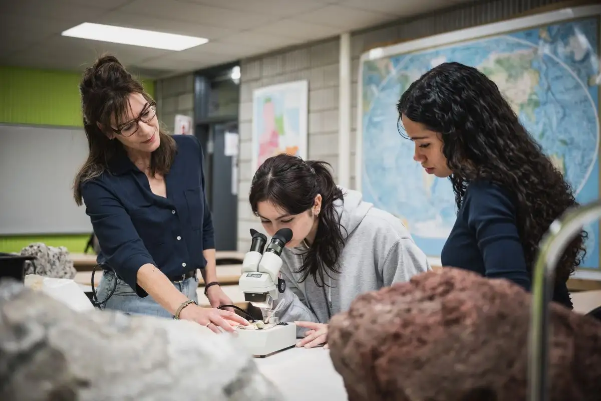 Personne étudiante qui regarde au microscope accompagnée de son enseignante