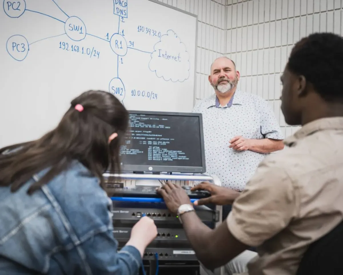 Personnes étudiantes en face l'ordinateur qui écoutent leur professeur au tableau