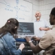 Personnes étudiantes en face l'ordinateur qui écoutent leur professeur au tableau