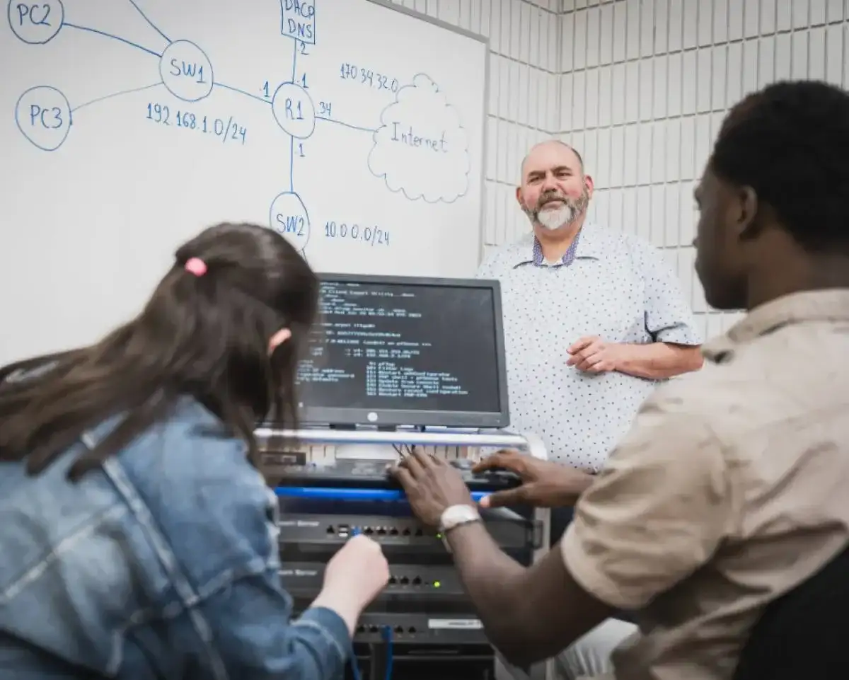 Personnes étudiantes en face l'ordinateur qui écoutent leur professeur au tableau
