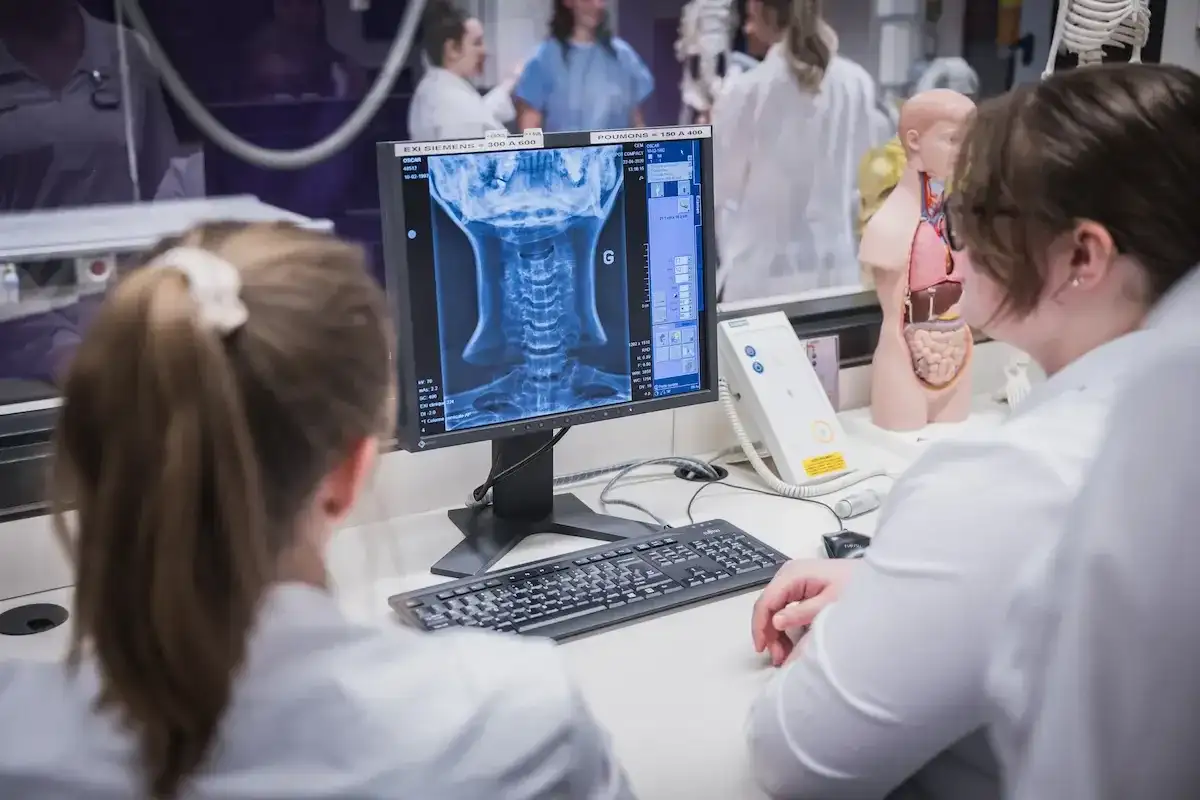 Deux personnes assises devant un ordinateur observent une radiographie du cou affichée à l’écran