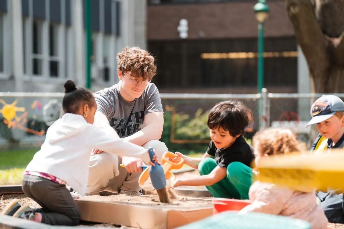 Étudiant qui joue avec des enfants dans un bac à sable