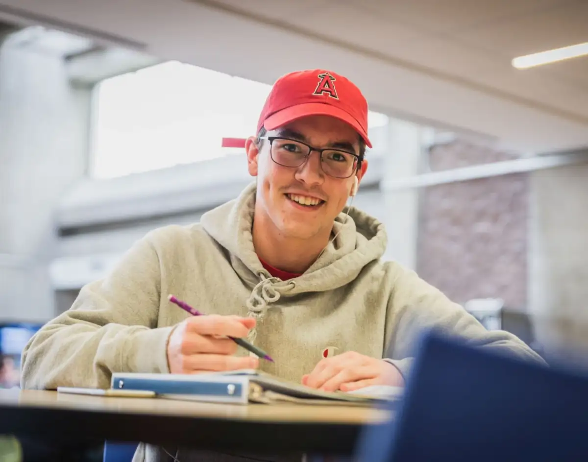 Personne étudiante à table qui sourit face caméra