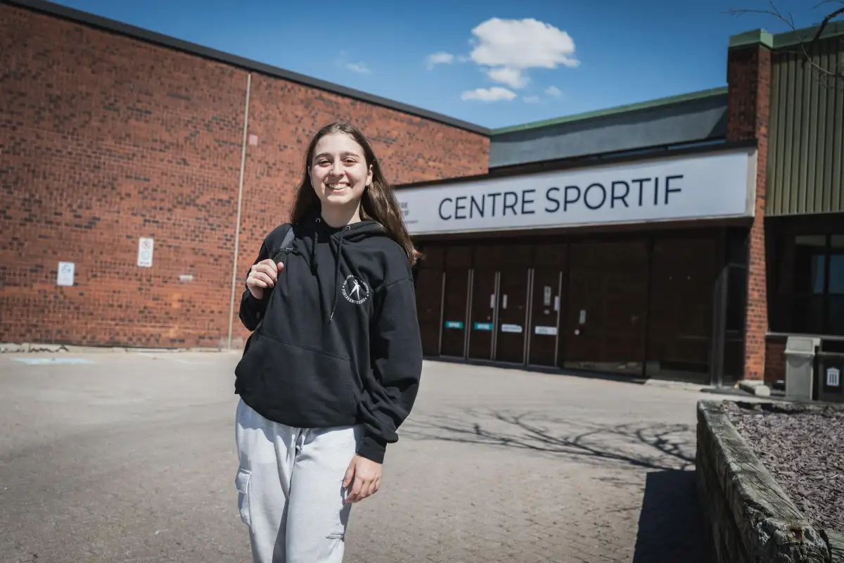 Personne étudiante devant l'entrée principale du centre sportif