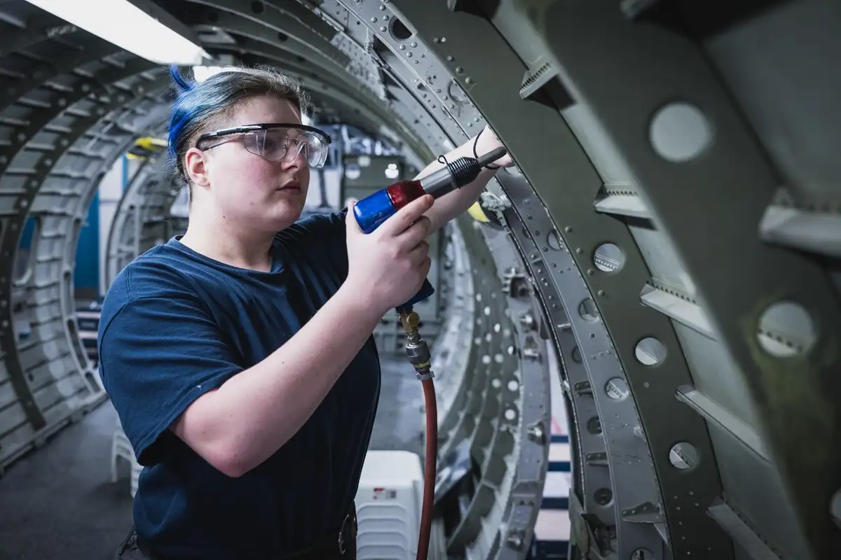 Etudiante posant un rivet dans un fuselage